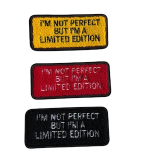 Peut inclure: Trois écussons rectangulaires avec le texte "I'M NOT PERFECT BUT I'M A LIMITED EDITION". Les écussons sont jaunes, rouges et noirs, chacun avec une bordure contrastante et du texte blanc.