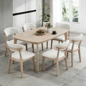 May include: A light wood dining table surrounded by six chairs. The chairs have light wood frames and curved backs with white, fluffy seat cushions. A decorative bowl and a cup of coffee sit on the table.