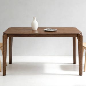 May include: A rectangular wooden dining table with a dark brown finish. A white vase and a plate with silverware are on the table. The table is supported by four legs. The table is approximately 60 inches long.