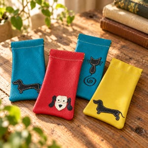 May include: Four rectangular leather pouches for glasses in blue, red, and yellow. One blue pouch features a black dachshund, the red pouch has a white and black dog face, the second blue pouch shows a black cat, and the yellow pouch has a black dachshund.