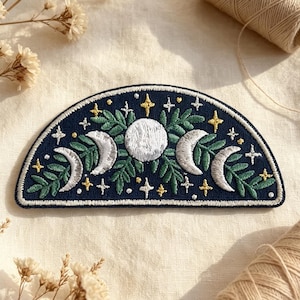May include: A semi-circular embroidered patch featuring a dark blue background with a central white full moon, silver crescent moons on either side, green leaves, and small yellow and white stars scattered across the design.