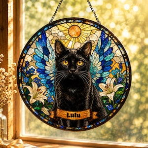 May include: A circular stained glass suncatcher featuring a black cat with yellow eyes and blue wings. The background includes a yellow sun, white clouds, and white lilies. A brown banner across the bottom displays the name Lulu in black text.