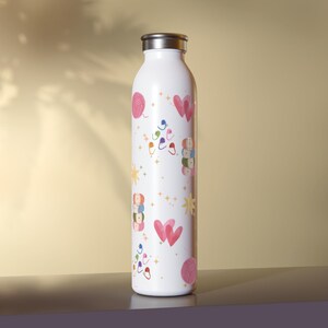 Könnte beinhalten: Weiße isolierte Wasserflasche mit silbernem Deckel. Die Flasche ist mit einem Muster aus rosa Wollknäueln, Herzen und bunten Stricknadeln verziert. Das Design wiederholt sich über die gesamte Oberfläche der Flasche.