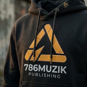 May include: A black hooded sweatshirt featuring a large yellow triangular graphic with a cracked texture. Below the triangle, the text 786MUZIK PUBLISHING is printed in white. The hoodie includes a drawstring hood with metal aglets and a small logo tag.