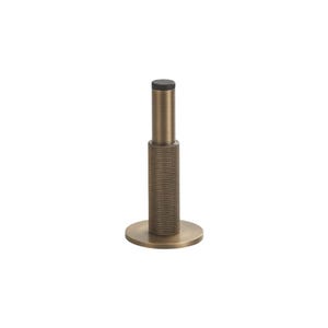 May include: A cylindrical door stop with a brushed bronze finish, featuring a textured knurled grip on the lower section and a smooth upper post topped with a small black rubber bumper for impact protection, mounted on a circular base plate.