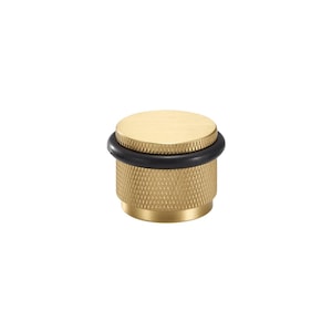 May include: A cylindrical door stop made of brushed brass with a smooth flat top and a textured diamond-patterned side. A thick black rubber ring is fitted around the middle of the brass body to provide a protective bumper for doors.