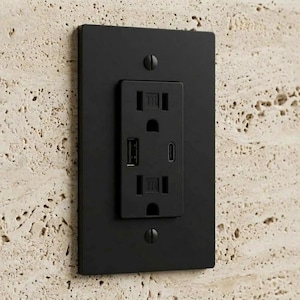 May include: A matte black rectangular electrical wall outlet cover plate featuring a standard duplex receptacle with two tamper-resistant slots, one USB-A port, and one USB-C port, secured by two matching black screws on a textured beige stone surface.