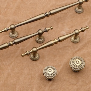 May include: An assortment of antique brass cabinet hardware, including several pull handles and two decorative knobs. The handles vary in size and feature a detailed, ornate design. The knobs have a floral pattern.
