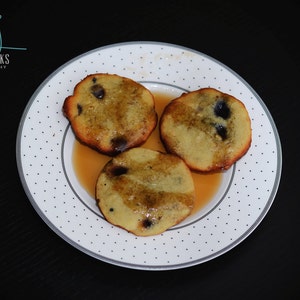 May include: Three golden brown pancakes with blueberries and a drizzle of syrup on a white plate with black polka dots.