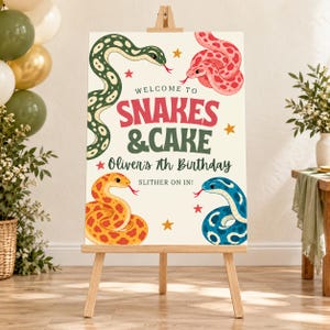 May include: A rectangular sign on a wooden easel featuring the text WELCOME TO SNAKES & CAKE Oliver's 7th Birthday SLITHER ON IN! The sign is decorated with illustrations of a green, pink, yellow, and blue snake and small yellow stars.