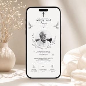 Puede incluir: Un teléfono inteligente que muestra un anuncio funerario digital para Martin David Johnson, con un retrato en blanco y negro, una cruz, dos palomas y gráficos de corona floral. El texto incluye fechas, una cita bíblica y detalles del evento.