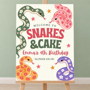 May include: A rectangular birthday sign on an easel featuring the text WELCOME TO SNAKES & CAKE Emma's 4th Birthday SLITHER ON IN! The design includes four colourful cartoon snakes in green, pink, orange, and purple, decorated with flowers and hearts.