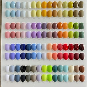 May include: A white display board featuring a grid of 120 individual nail polish color samples. Each sample is a smooth, rounded, glossy or matte plastic nail tip arranged in rows, with small black numerical labels printed below each item.