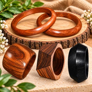 Puede incluir: Una colección de cinco pulseras de madera que incluye dos brazaletes circulares lisos en un tono marrón rojizo cálido, dos brazaletes anchos facetados con vetas de madera visibles y un brazalete facetado negro sólido con acabado pulido.