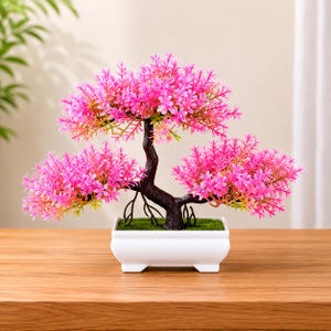 Op de afbeelding: Een decoratieve kunstmatige bonsai boom met felroze bladeren en een donkerbruine stam. De boom staat in een witte rechthoekige pot gevuld met groen mos. De bonsai is een miniatuur replica van een boom.