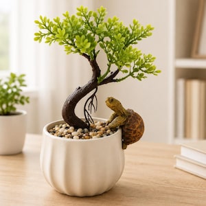 May include: A small artificial bonsai tree with bright green leaves and a dark brown trunk, planted in a white, ribbed ceramic pot filled with small, multi-colored pebbles. A brown, textured turtle figurine is perched on the rim of the pot.