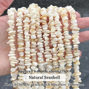 May include: Multiple strands of off-white, irregular, tumbled natural seashell beads. The text on the image reads: Approx: 8-10mm about 129pcs, Natural Seashell, Photo By Mobile: Each Batch May Have Difference.