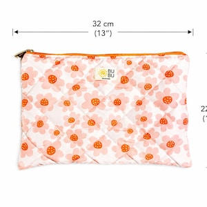 May include: A quilted pouch featuring a floral pattern, with a gold zip. The pouch is white with pink and orange flower designs. It measures 32 cm wide and 22 cm high. The label reads "BU BU Handmade".