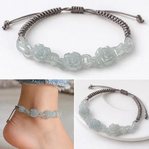 May include: A bracelet featuring three carved pale green jade rose beads connected by a grey woven cord. The adjustable cord has a sliding knot closure with two small knotted ends. The design showcases a floral motif with smooth, polished stone.