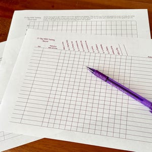 Op de afbeelding: Een wit 21-daags ADHD-trackingformulier op papier met een rasterindeling voor dagelijkse symptoommonitoring, inclusief kolommen voor datum, medicatie, slaap en diverse symptomen, vergezeld door een paarse balpen die op het document rust.
