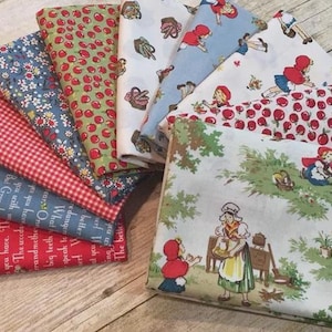 May include: A collection of folded fabric squares featuring various patterns including red and white gingham, floral prints, cherry motifs, and illustrations of Little Red Riding Hood with text excerpts from the classic fairy tale story.