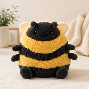 May include: A soft bumblebee toy with a rounded shape, featuring black and yellow stripes. It has small black antennae, a smiling face, and tiny black limbs. The wings are a light cream colour. The toy is designed to be cuddly.