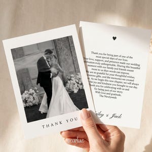 以下が含まれることがあります： 屋外で抱き合うカップルの白黒写真が印刷された白い結婚式のサンキューカード。カードの下部にはThank Youの文字があり、BaileyとJackの署名と小さなハートのアイコンが入った感謝のメッセージが印刷されています。