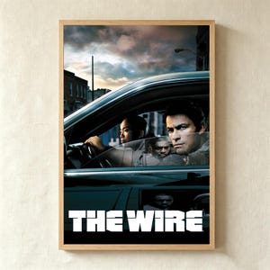以下が含まれることがあります： テレビシリーズ「THE WIRE」のシーンを描いた額入りポスター。夕暮れ時の街を背景に、暗い車内にいる3人の人物が写っている。下部には「THE WIRE」というタイトルが大きく太い白のアルファベットで印刷されている。