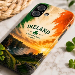 Könnte beinhalten: Eine Smartphone-Hülle mit einer irischen Küstenlandschaft bei Sonnenuntergang, inklusive Klippen und Ruinen. Unter einem grünen Kleeblatt steht der Text IRELAND und ERIN GO BRAGH. Das Design zeigt die Farben Grün, Weiß und Orange der irischen Flagge.