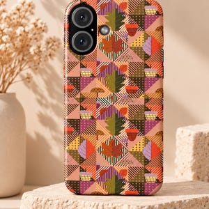 Könnte beinhalten: Eine Smartphone-Hülle mit einem sich wiederholenden geometrischen Muster aus Dreiecken und Quadraten in Orange-, Braun-, Lila- und Grüntönen. Das Design zeigt stilisierte Herbstblätter, Eicheln und kleine Pilze vor einem Hintergrund aus Streifen und Punkten.
