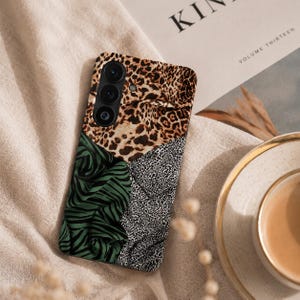 Könnte beinhalten: Eine rechteckige Smartphone-Hülle mit einem mehrteiligen Muster. Der obere Bereich zeigt ein braun-schwarzes Leopardenmuster, unten links ein dunkelgrün-schwarzes Zebramuster und unten rechts ein kleines schwarz-weißes Punktemuster.