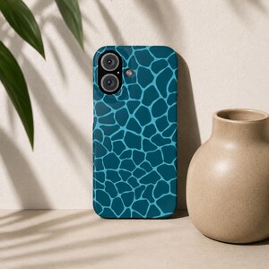 Könnte beinhalten: Eine Smartphone-Hülle mit einem von Giraffen inspirierten Muster in Dunkel-Türkis und Hellblau. Die Hülle verfügt über eine Aussparung für die Doppelkamera in der oberen linken Ecke und eine glatte, glänzende Oberfläche mit geometrischem Design.