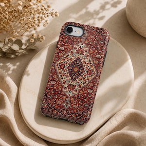 Könnte beinhalten: Eine Handyhülle mit einem detaillierten, verzierten Teppichdesign in Rot-, Creme- und Marineblautönen. Die Hülle hat ein zentrales Medaillon und florale Muster und bietet eine Vintage-Ästhetik. Die Hülle liegt auf einem weißen Teller.