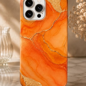 Könnte beinhalten: Eine Smartphone-Hülle mit einem leuchtend orangefarbenen Marmormuster und wirbelnden, flüssigkeitsähnlichen Texturen. Das Design wird durch unregelmäßige, schimmernde Blattgoldakzente und feine goldene Adern auf dem orangefarbenen Hintergrund ergänzt.
