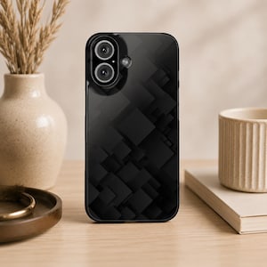 Puede incluir: Funda de teléfono negra con un patrón geométrico de cuadrados. La funda tiene un acabado brillante y un recorte para una cámara de doble lente. La funda del teléfono está sobre una superficie de madera, con un jarrón y una taza en el fondo.