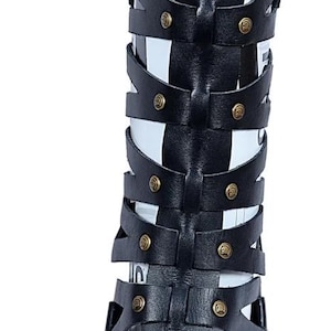 May include: Black leather gladiator sandals with multiple straps and gold-colored rivets. The sandals have an open toe design and a white sole. The tall design extends up the leg, offering a unique style.