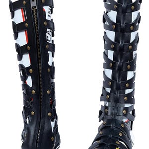 May include: Black and white gladiator sandals with a zipper and strap design. The sandals have a flat sole with white and black stripes. The sandals have the word "CA" printed on the side.