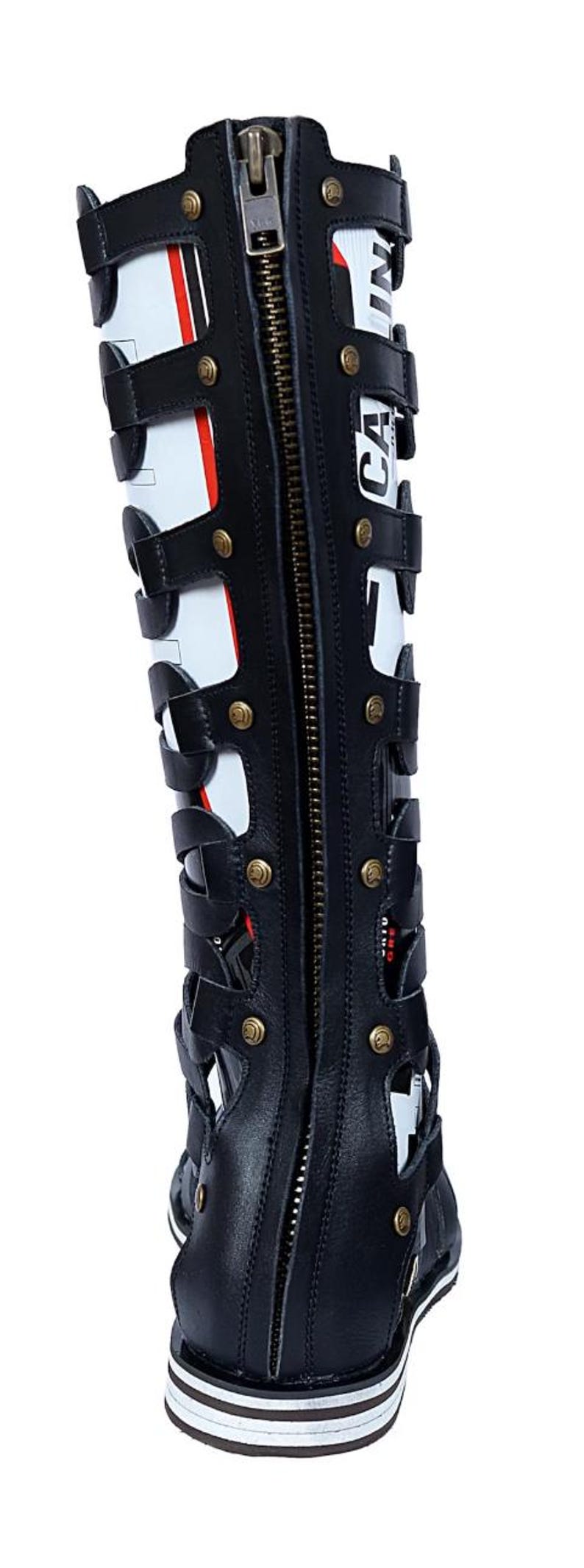 May include: Black and white knee-high gladiator boot with a full-length zipper and gold-colored rivets. The boot features a series of straps and cutouts, with the word "CA" visible on the side.