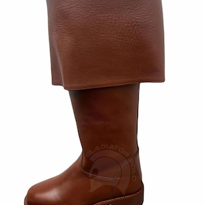 May include: A brown leather boot featuring a wide, folded-over cuff at the top and a rounded toe. The side of the boot displays a faint embossed logo with the text GLADIATOR POLO and a graphic of a helmet. The boot has a flat sole and stitching.