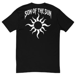 Può includere: Una t-shirt nera a maniche corte con una grafica bianca sul retro. Il disegno mostra un sole stilizzato con raggi curvi e il testo SON OF THE SUN arcuato sopra in un carattere tipografico audace, nitido e dai bordi appuntiti.