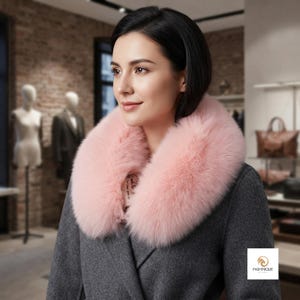Puede incluir: Un abrigo gris oscuro con un cuello grande y esponjoso de piel sintética de color rosa claro. El abrigo tiene un diseño de solapa estructurado y una textura de tela mate y suave. Un pequeño logotipo cuadrado blanco con el texto PASHMIQUE BY KOTA.