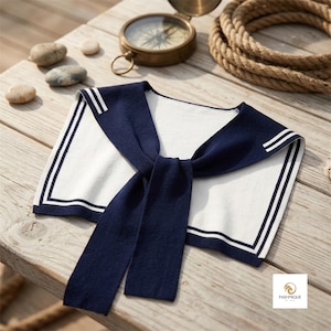 Pode incluir: Um colarinho de estilo marinheiro branco com uma borda azul-marinho e duas listras brancas finas. O colarinho apresenta uma gravata longa azul-marinho que pende do centro. O design é limpo e simples, com uma estética e cores náuticas clássicas.