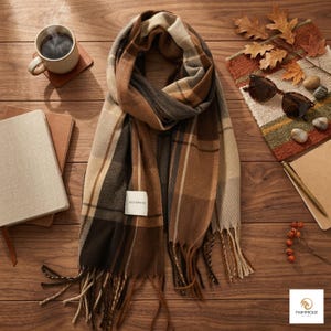 Peut inclure: Une écharpe à carreaux présentant une palette de couleurs marron, beige, crème et gris anthracite. L'écharpe a une forme rectangulaire avec des extrémités à franges et une petite étiquette rectangulaire blanche cousue portant l'inscription SELF SERVICE.