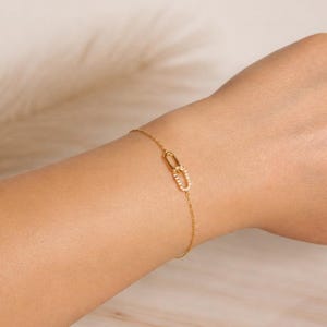 May include: A delicate gold bracelet featuring a double-link design. One link is adorned with small, sparkling crystals. The bracelet is shown on a wrist, showcasing its elegant and minimalist style.
