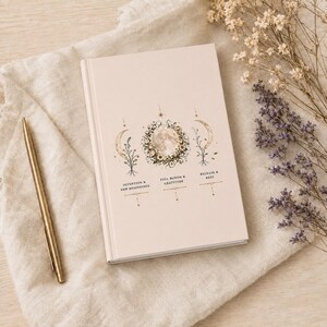 Könnte beinhalten: Ein hellbeiges Notizbuch mit einer zentralen Abbildung eines Mondes, umgeben von Blumen, flankiert von zwei Mondsicheln und botanischen Stielen. Der Text lautet: INTENTION & NEW BEGINNINGS, FULL BLOOM & GRATITUDE und RELEASE & REST.