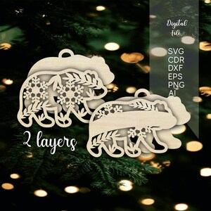 May include: A two-layer wooden bear ornament featuring intricate cutouts of snowflakes and foliage. The design includes a top layer with detailed patterns and a solid bottom layer. Text on the image reads Digital File, SVG, CDR, DXF, EPS, PNG, AI, 2 layers.