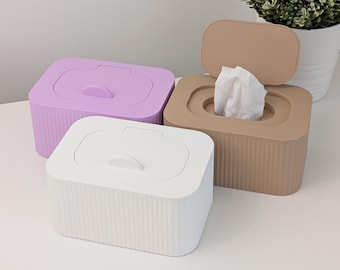 Könnte beinhalten: Drei rechteckige Taschentuchspender mit abgerundeten Ecken und vertikal gerippten Seiten. Einer ist weiß, einer hellviolett und einer beige. Der beige Spender hat einen offenen Deckel, aus dem ein weißes Taschentuch herausragt.