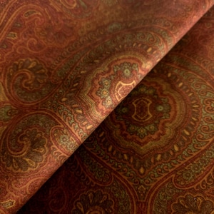 May include: A fabric featuring a dense, intricate paisley pattern in shades of deep rust, burnt orange, and muted olive green. The design consists of repeating teardrop and floral motifs arranged in a symmetrical, ornate layout across the surface.