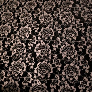 May include: A black fabric featuring an intricate white floral lace overlay. The pattern consists of repeating, detailed flower motifs connected by delicate, thin lace webbing, creating a high-contrast visual texture across the entire surface.
