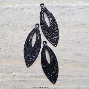 May include: Three black metal pendant charms in the shape of a leaf with an intricate design. The charms have a cutout in the center.